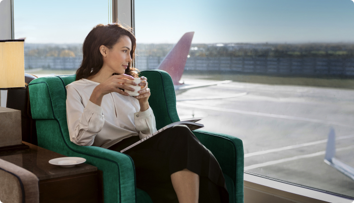 Frau mit Kaffee in der Hand sitzt in derAirport-Lounge und schaut auf die Start- und Landebahn